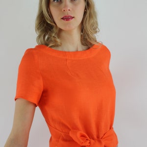 May include: A woman wearing a bright orange linen dress with a self-tie sash at the waist.