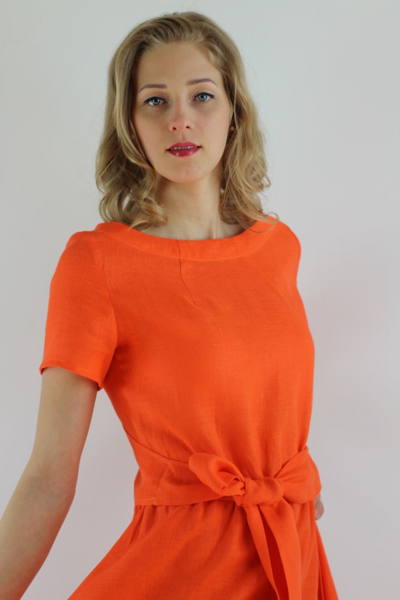 May include: A woman wearing a bright orange linen dress with a self-tie sash at the waist.