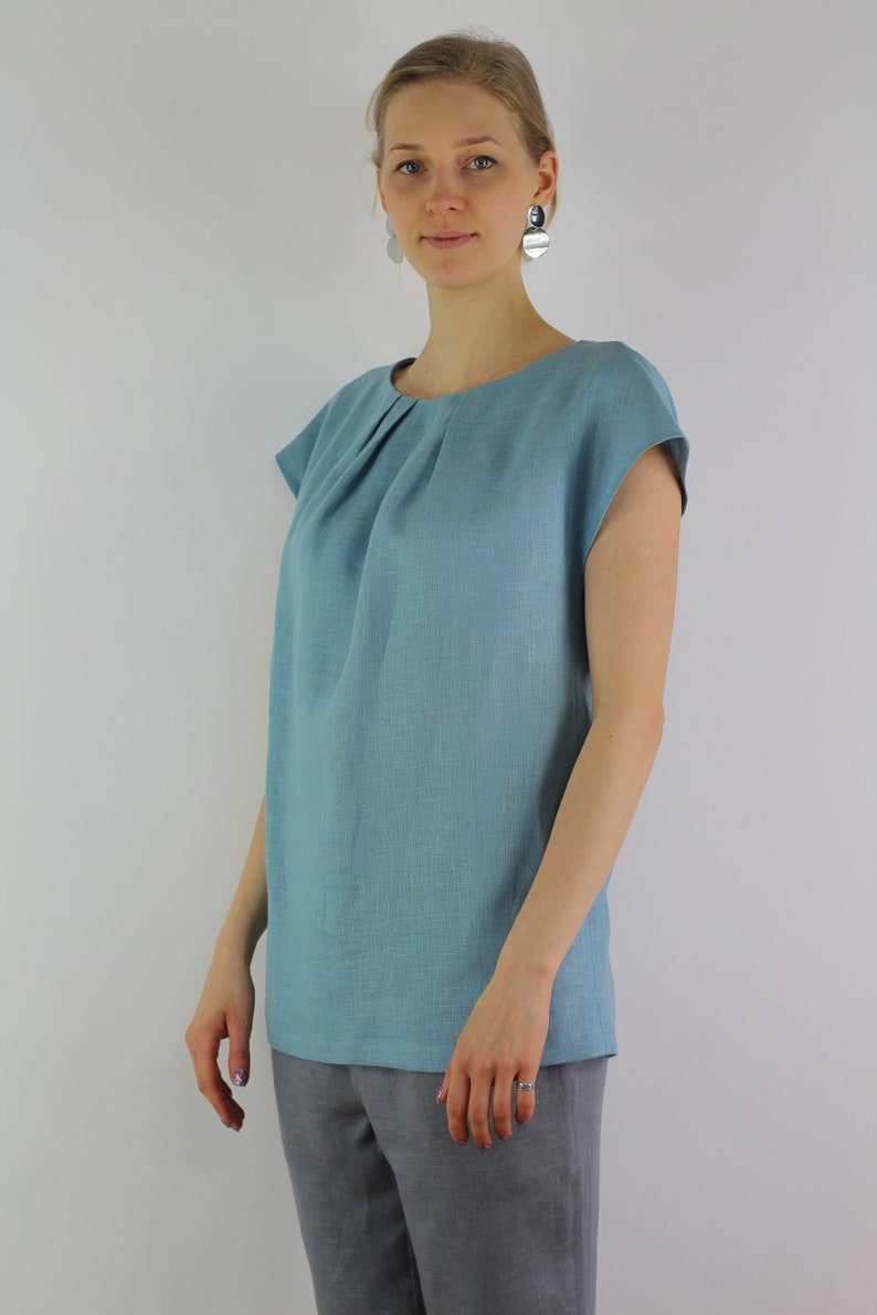 May include: A light blue linen top with a gathered neckline and short sleeves.