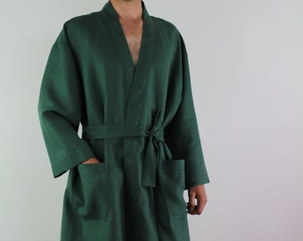 May include: A dark green linen robe with a shawl collar, long sleeves, and a waist tie. The robe has two front pockets and is knee-length. The fabric appears to be a solid color. The robe is worn by a person.