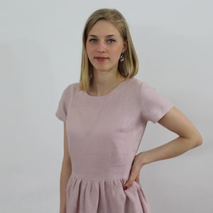 K&ouml;nnte beinhalten: Eine Frau tr&auml;gt ein hellrosa Leinenkleid mit kurzen &Auml;rmeln und einem runden Ausschnitt. Das Kleid hat einen gerafften Rock.