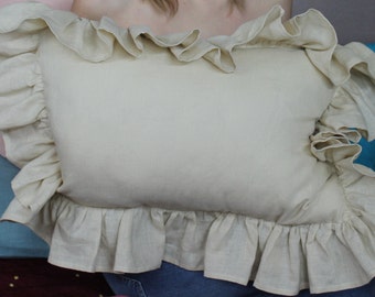 Puede incluir: Una almohada de color crema con un borde con volantes. La almohada está hecha de una tela de lino suave.