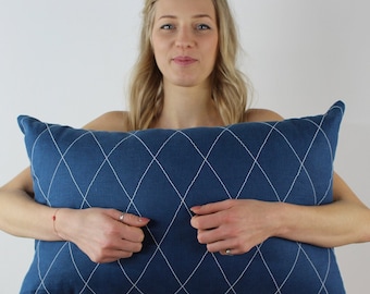 Könnte beinhalten: Ein blaues Kissen mit weißen Rauten-Steppnähten. Das Kissen wird von einer Person gehalten.