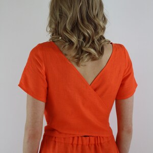 May include: A bright orange linen dress with a wrap-style top and a skirt. The dress has short sleeves and a V-neckline.
