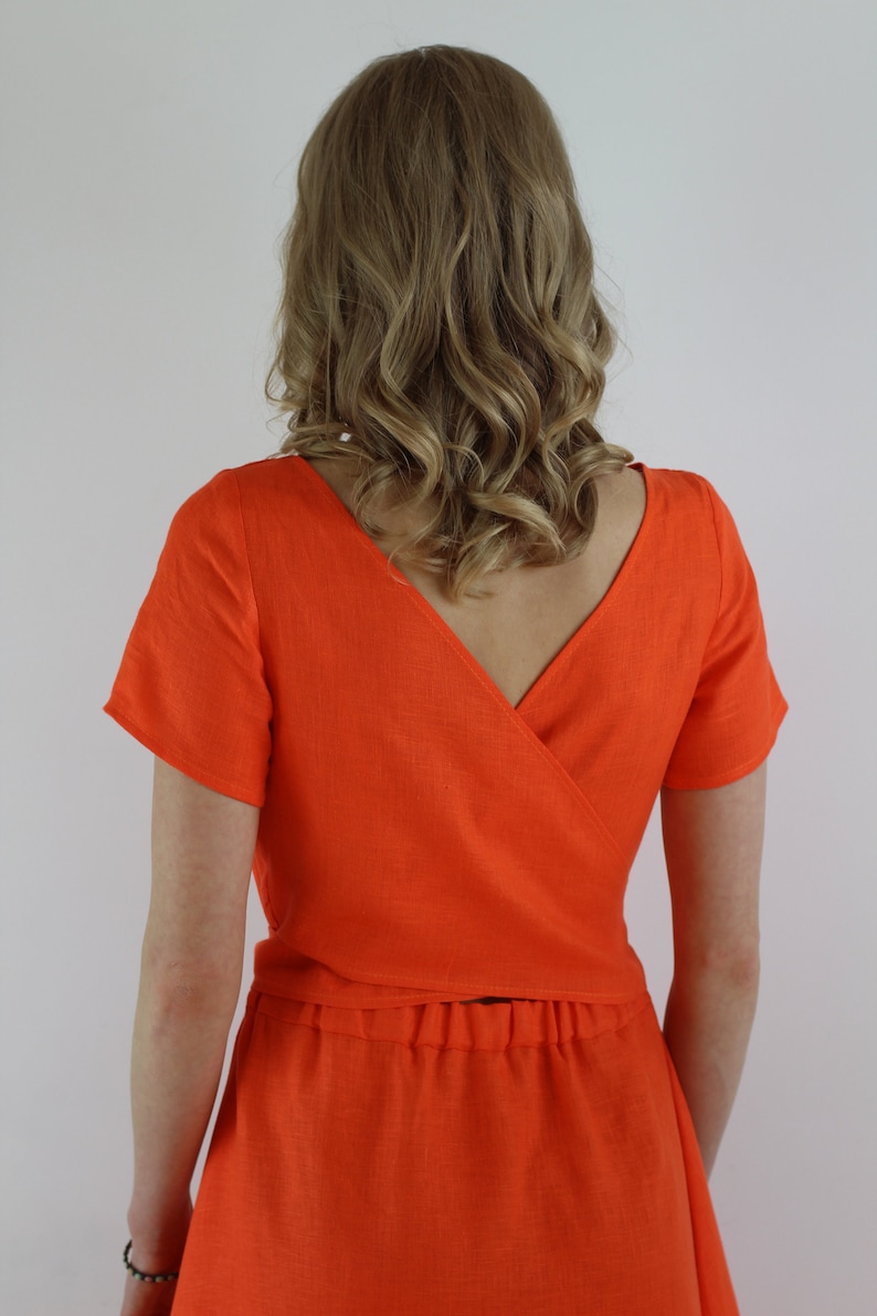May include: A bright orange linen dress with a wrap-style top and a skirt. The dress has short sleeves and a V-neckline.