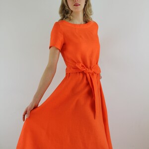 May include: A bright orange linen dress with a short sleeve and a tie at the waist.