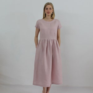 K&ouml;nnte beinhalten: Ein hellrosa Leinenkleid mit kurzen &Auml;rmeln und einem gerafften Rock. Das Kleid hat einen runden Ausschnitt und Taschen an den Seiten.