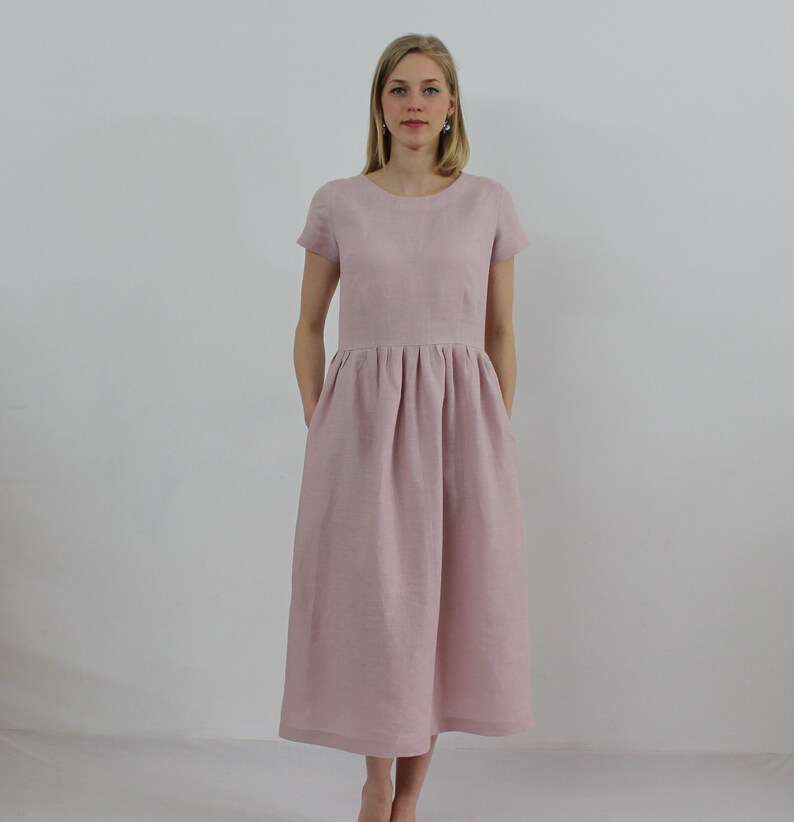 K&ouml;nnte beinhalten: Ein hellrosa Leinenkleid mit kurzen &Auml;rmeln und einem gerafften Rock. Das Kleid hat einen runden Ausschnitt und Taschen an den Seiten.