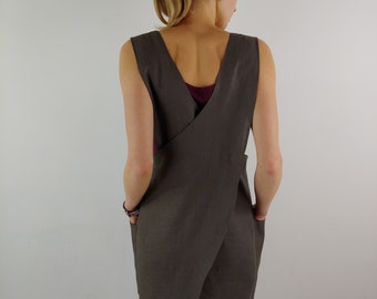 May include: A grey linen apron with a criss-cross back design and two pockets. The apron is long and reaches below the knees.