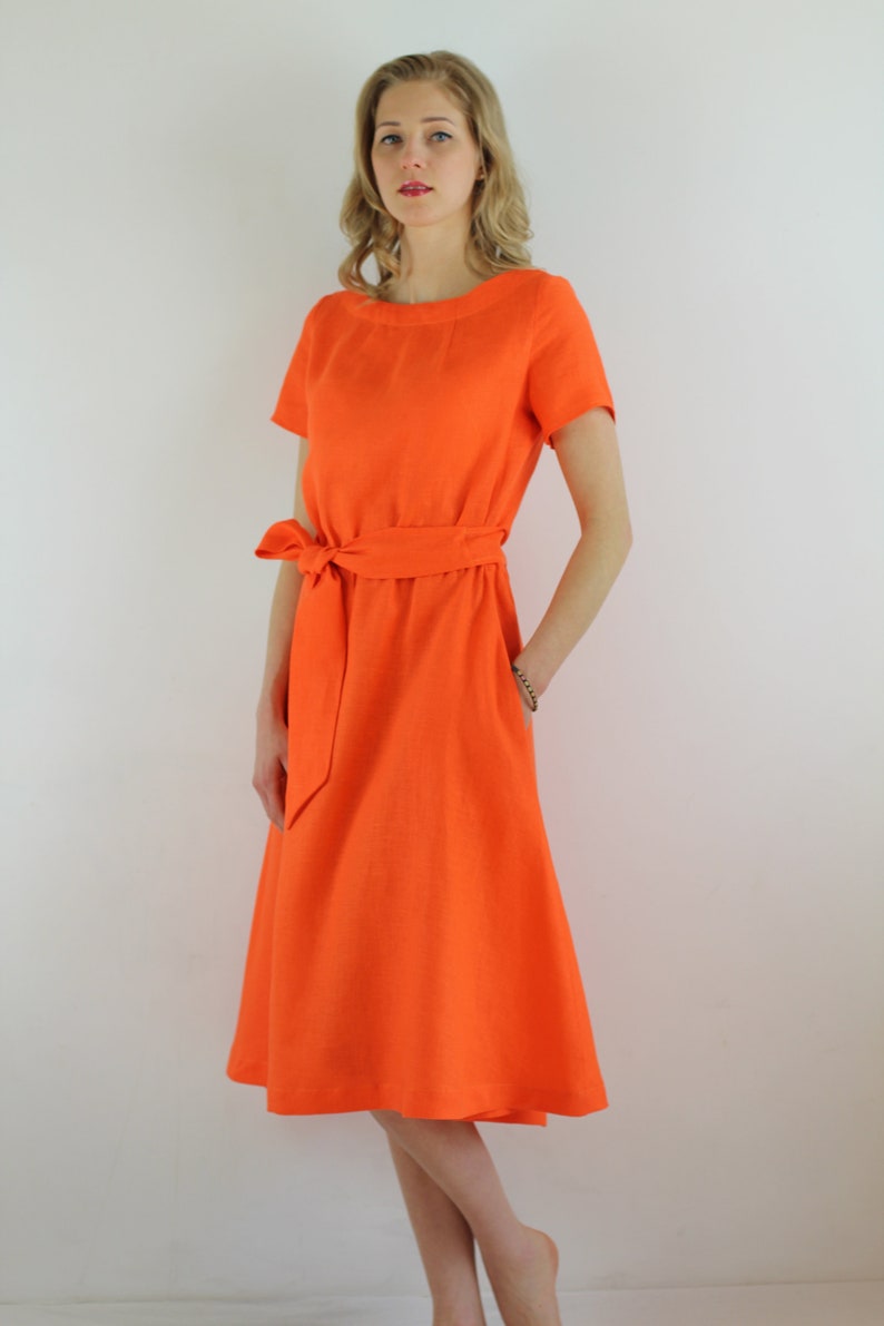 May include: A bright orange linen dress with a short sleeve and a tie belt. The dress has a simple, classic design.