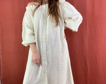 Puede incluir: Un vestido blanco de lino sin hombros con botones en la parte delantera y un dobladillo con volantes.