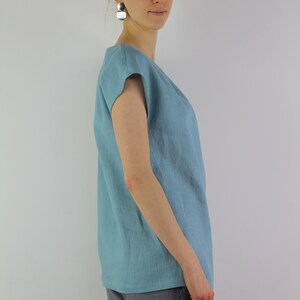 May include: A light blue linen top with short sleeves. The top has a relaxed fit and a slightly rounded neckline.