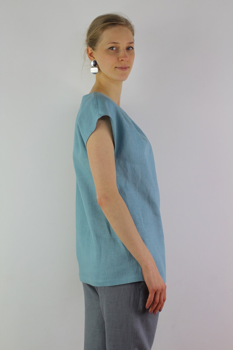 May include: A light blue linen top with short sleeves. The top has a relaxed fit and a slightly rounded neckline.