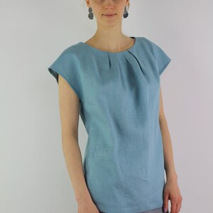 May include: A light blue linen top with a pleated neckline and short sleeves. The top is loose-fitting and has a relaxed silhouette.