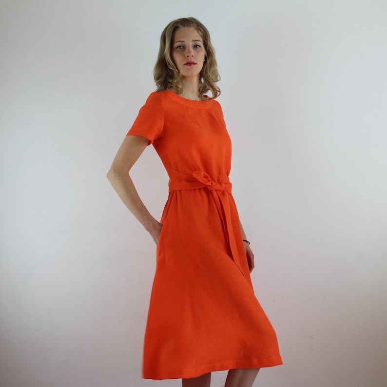 May include: A bright orange linen dress with a short sleeve and a tie at the waist.