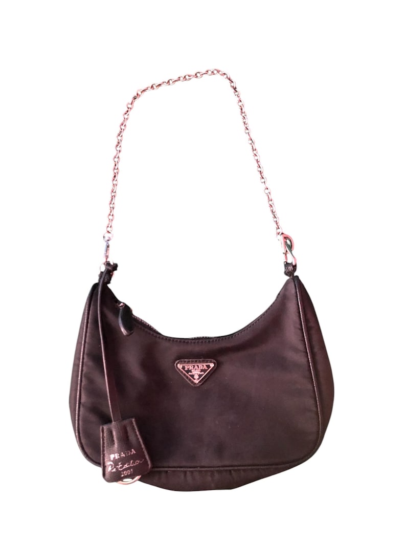 May include: A dark brown nylon Prada Re-Edition 2001 shoulder bag with a silver chain strap and a small leather tag that says "Prada Re-Edition 2001".