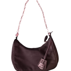 May include: A dark brown nylon shoulder bag with a silver chain strap and a silver zipper. The bag has a small silver tag with the text "PRADA" on it.