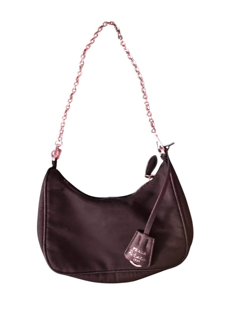 May include: A dark brown nylon shoulder bag with a silver chain strap and a silver zipper. The bag has a small silver tag with the text "PRADA" on it.