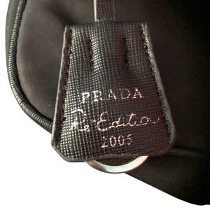 May include: A black leather bag with a silver ring and a Prada label that reads "Prada Limited Edition 2005".
