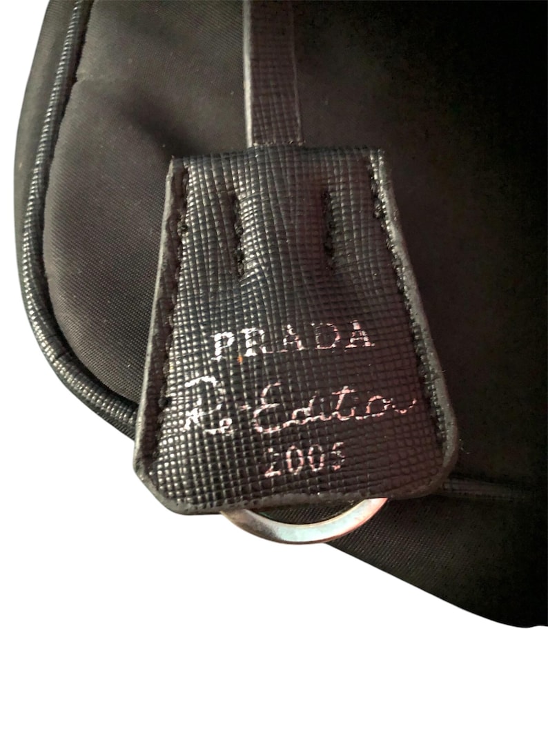 May include: A black leather bag with a silver ring and a Prada label that reads "Prada Limited Edition 2005".