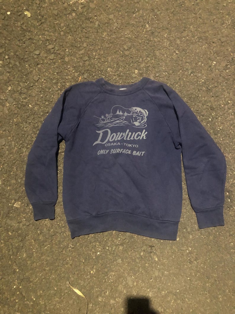 May include: Navy blue sweatshirt with the text "Dowluck OSAKA-TOKYO ONLY SURFACE BAIT" in a light grey color. The sweatshirt has long sleeves and a crew neck.