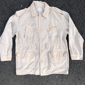 May include: A beige utility jacket with multiple pockets and a drawstring waist.