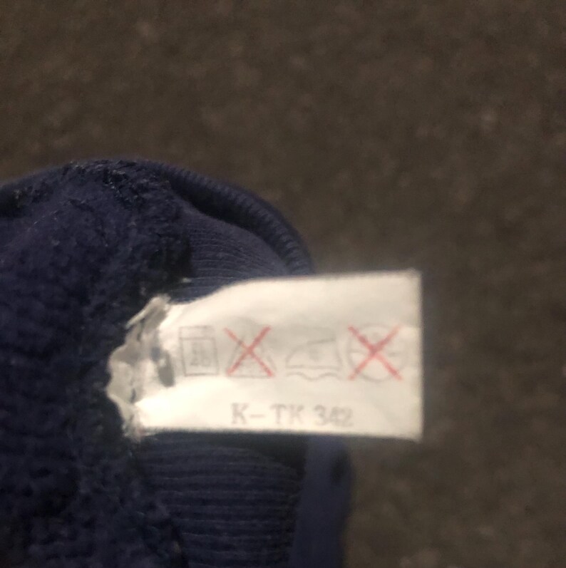 May include: Close-up of a navy blue fabric with a white tag attached. The tag has care symbols and the text "K-TK 342". The fabric appears to be a knit material.