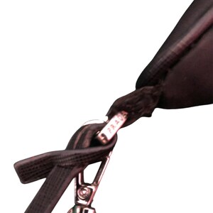 May include: Close-up of a black leather strap with a silver clasp and a silver tag that reads "PRADA" on a black bag.