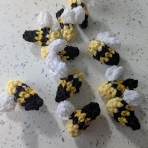 May include: A collection of eight crocheted bumblebees with black and yellow striped bodies and white wings.