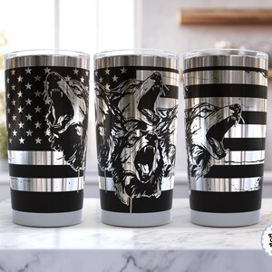 May include: Three stainless steel tumblers with black and silver designs. One tumbler features a black and silver American flag design with a howling wolf. The other two tumblers have howling wolf graphics and black stripes.