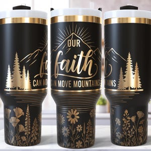May include: Black travel tumbler with a white lid and gold accents. The tumbler features a gold design with the text "Our faith can move mountains", mountains, trees, and flowers. The tumbler has a black handle.