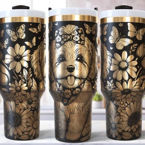 Puede incluir: Vaso térmico negro y dorado con una ilustración de perro y diseños florales y de mariposas. El vaso tiene un asa negra y un borde blanco y dorado. El diseño incluye girasoles y mariposas.