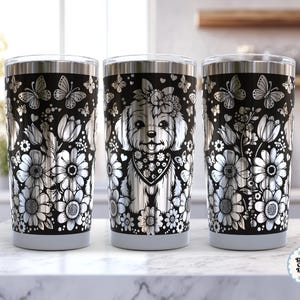 Puede incluir: Tres tazas de viaje de acero inoxidable con fondo negro. Las tazas presentan un diseño floral y de mariposas en plata, con una imagen central de un perro con pañuelo y corona de flores. El diseño se repite en cada taza.