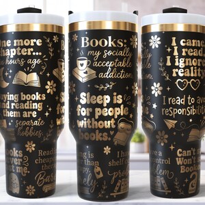 Op de afbeelding: Drie zwarte reisbekers met gouden tekst en accenten. Elke beker heeft een ander citaat over boeken en lezen. De bekers hebben zwarte handvatten, witte randen en zwarte deksels. De bekers zijn versierd met bloemen en boekgerelateerde afbeeldingen.