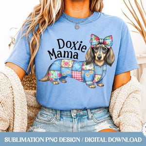 Może przedstawiać: Jasnoniebieska koszulka z ilustracją jamnika z patchworkowym wzorem i kokardą. Tekst "Doxie Mama" znajduje się nad psem. Koszulka jest do pobrania cyfrowo.