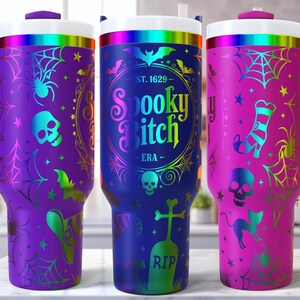May include: Three Halloween-themed travel mugs with handles. The mugs are purple, blue, and pink, each featuring spooky designs like spiders, skulls, bats, and the text "Spooky Bitch". They have white lids with a rainbow band.