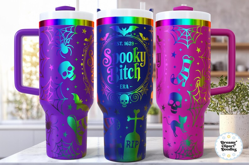 May include: Three Halloween-themed travel mugs with handles. The mugs are purple, blue, and pink, each featuring spooky designs like spiders, skulls, bats, and the text "Spooky Bitch". They have white lids with a rainbow band.