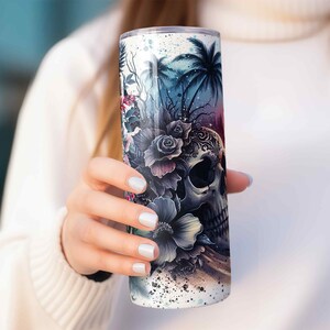 May include: A white stainless steel tumbler with a colorful design featuring a skull with flowers and palm trees.
