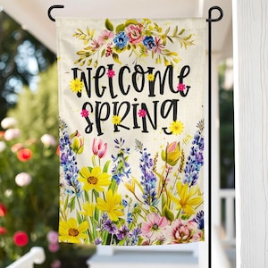 May include: A welcome spring garden flag with a floral design featuring yellow, pink, purple, and blue flowers. The flag has the text "Welcome Spring" in black lettering.