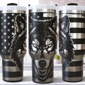 May include: Black and silver travel mugs with a wolf design. The mugs feature a black handle, a white lid, and a design that incorporates the American flag and a wolf's face. The mugs are approximately 8 inches tall.