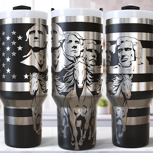 May include: Three black and silver travel mugs with a handle. The mugs feature images of U.S. presidents, the American flag, and horses. The mugs have a black handle and a white lid. The design is etched into the silver bands.
