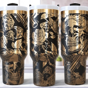 Könnte beinhalten: Schwarzer und goldener isolierter Reisebecher mit Griff. Der Becher hat ein detailliertes Design aus Totenköpfen, Rosen, Würfeln und Pistolen. Der Deckel ist weiß mit einem goldenen Band, und der Griff ist schwarz. Das Design wiederholt sich auf allen drei Bechern.