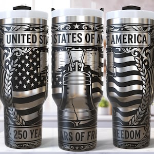 May include: Stainless steel travel mugs with black handles and white lids. The mugs feature engraved designs of the American flag, the Liberty Bell, and the text "UNITED STATES OF AMERICA", "250 YEARS OF FREEDOM".