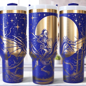 May include: Blue and gold insulated travel mug with a handle. The design features a knight riding a skeletal horse, a dragon, and a starry night sky. The mug has a white lid and a blue handle.