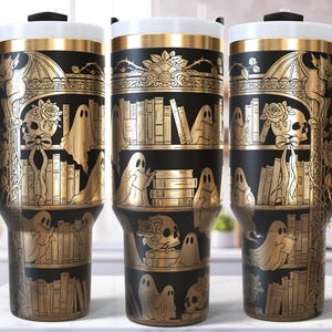 Könnte beinhalten: Schwarze und goldene Reisebecher mit einem gruseligen Bibliotheksdesign. Das Design zeigt Geister, Totenköpfe, Bücher und florale Akzente. Der Becher hat einen schwarzen Griff und einen weißen und goldenen Deckel. Höhe ca. 20 cm.