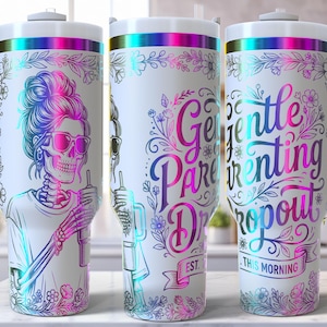 May include: White tumbler with a wraparound design featuring a skeleton with sunglasses and the text "Gentle Parenting Dropout." The design includes floral accents and a rainbow color scheme. The tumbler has a white handle and lid.