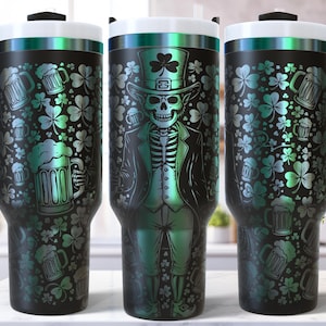 May include: Black and green insulated tumbler with a handle, featuring a skeleton in a green suit and top hat, surrounded by shamrocks and beer mugs. The tumbler has a white lid and a black handle.