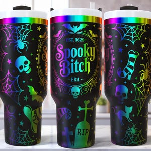 May include: Black tumbler with a handle, featuring a Halloween design. The design includes spiders, cobwebs, bats, skulls, and the text "Spooky Bitch - ERA" in a colorful, rainbow gradient. The tumbler has a white rim and a black handle.
