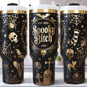 May include: Black and gold Halloween-themed tumbler with a white lid and black handle. The tumbler features spiderwebs, bats, skulls, and the text "Spooky Bitch - ERA". A spooky and fun accessory for Halloween.