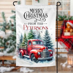 May include: A white Christmas garden flag with a red truck carrying a Christmas tree. The flag reads "Merry Christmas From The Petersons Family".